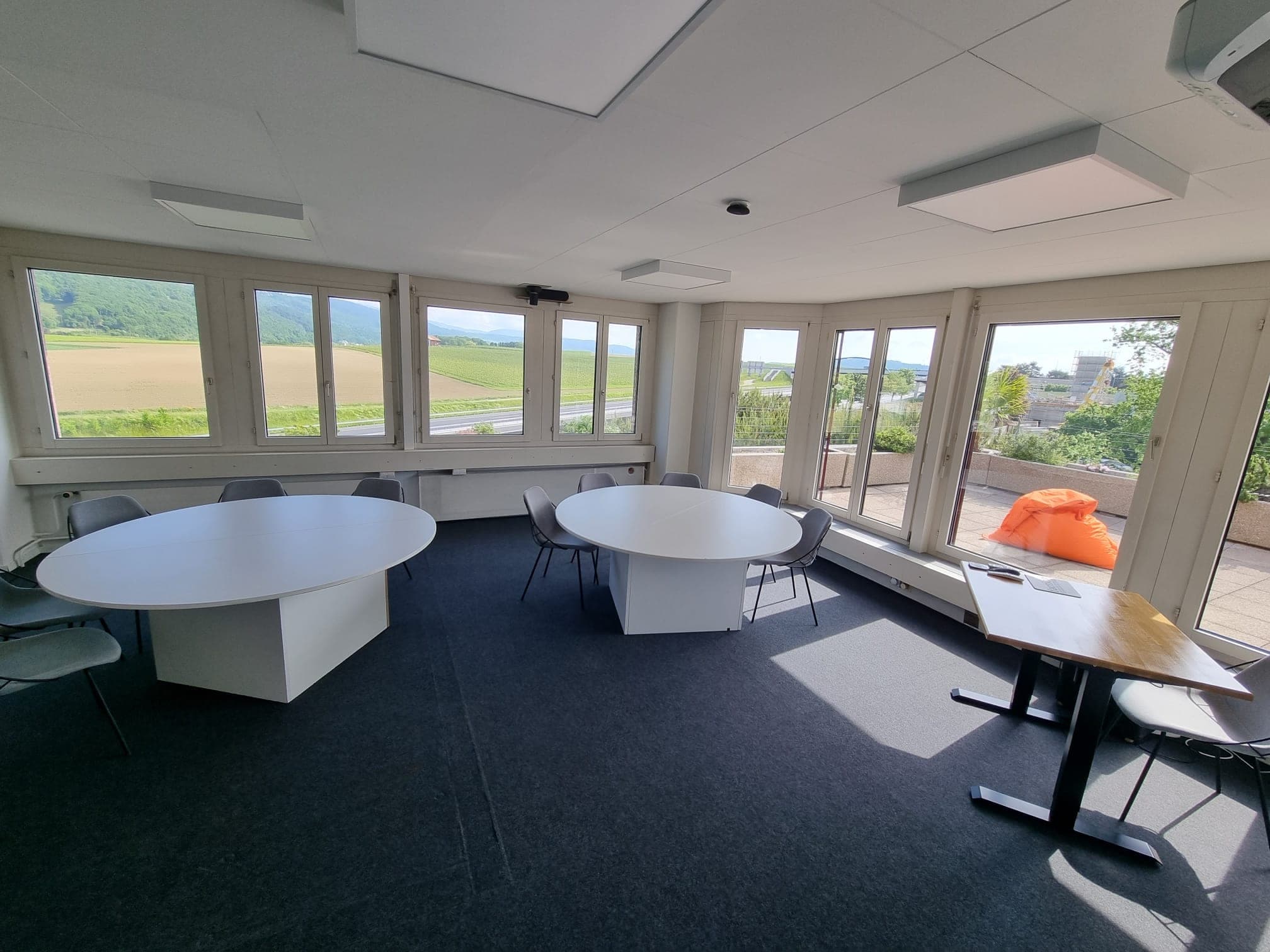 La salle Fléchettes avec ses deux grandes tables rondes et sa baie vitrée sur la campagne